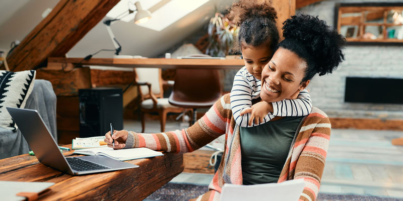 woman in front of computer with child hugging her