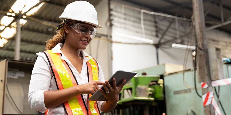 woman in hard hat and vest reviewing a tablet